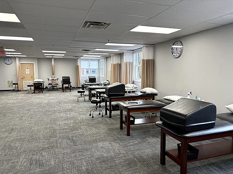 The Denville, NJ treatment floor at Carroll Physical Therapy, with padded tables, privacy curtains and anatomy wall charts on the wall