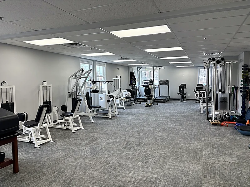 The exercise floor at the Carroll Physical Therapy clinic in Denville, NJ, with white-framed weight machines, a treadmill, a recumbent bike, a cable tower, and exercise balls along the far wall