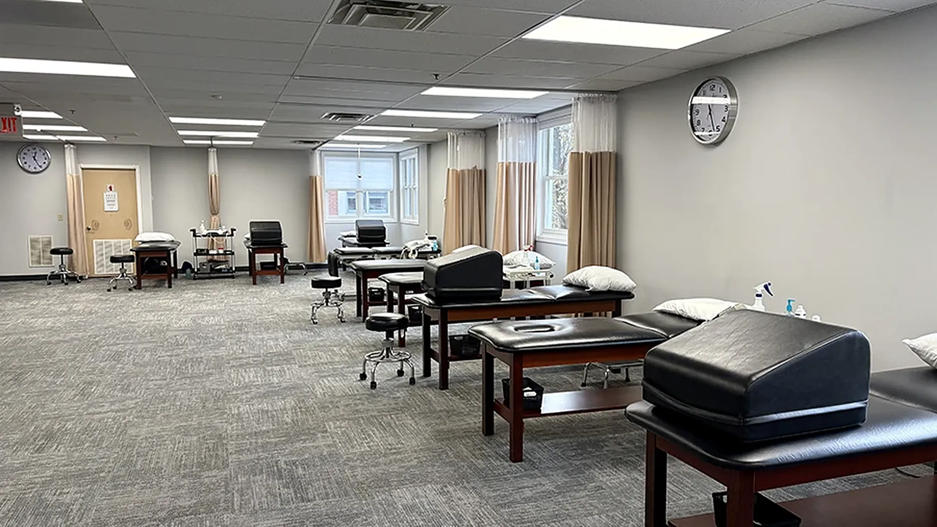 The open treatment floor at the Denville clinic, with padded tables in a row, privacy curtains at the windows, and wall clocks
