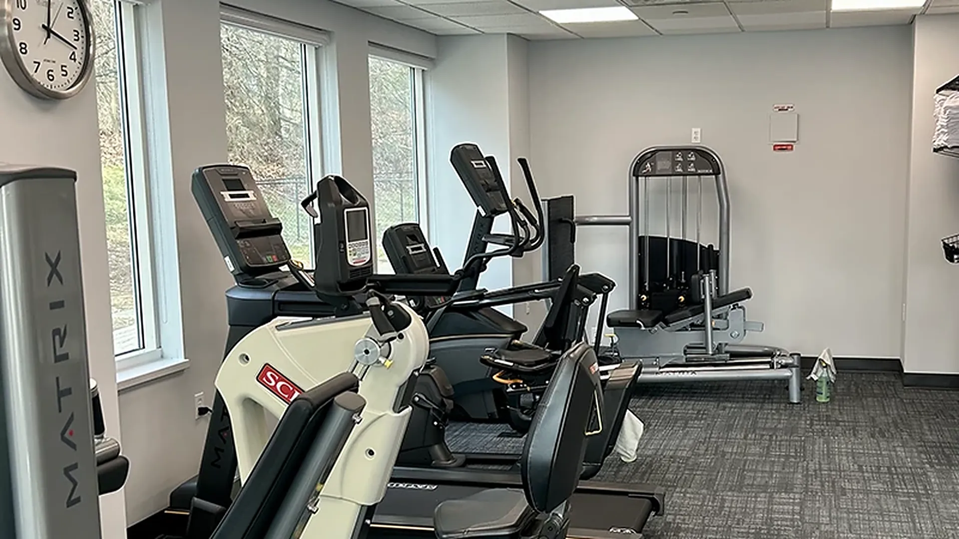 The conditioning corner at Carroll Physical Therapy with a recumbent bike, elliptical, and a seated leg press machine under a wall clock