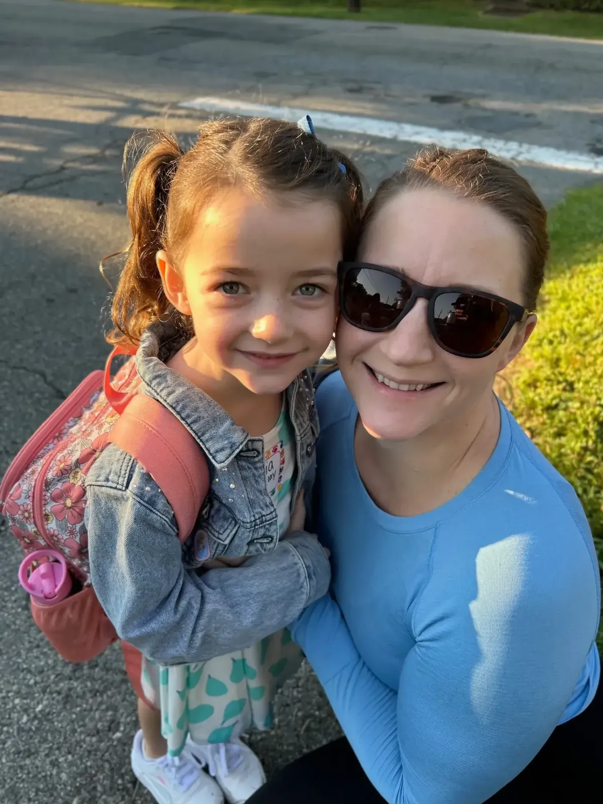 Dan Streeter's young daughter with pigtails and a pink backpack, cheek to cheek with her mother in a selfie on their street